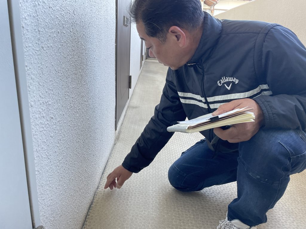 共用廊下の壁の足元を手で確かめる職人
